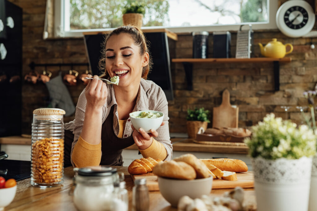 Smiling woman tasting food while cooking in the kitchen.